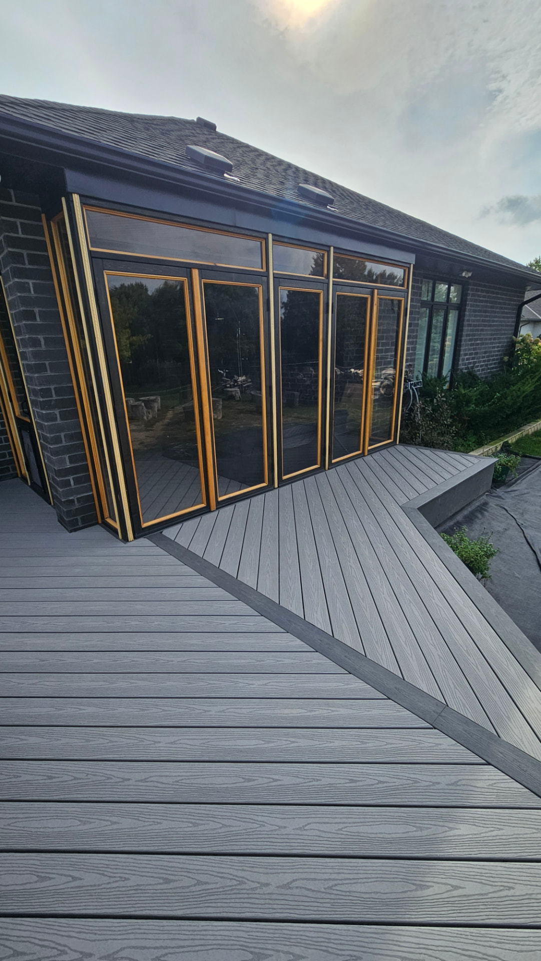 Grey composite deck with contrasting dark border wrapping a four-season sunroom