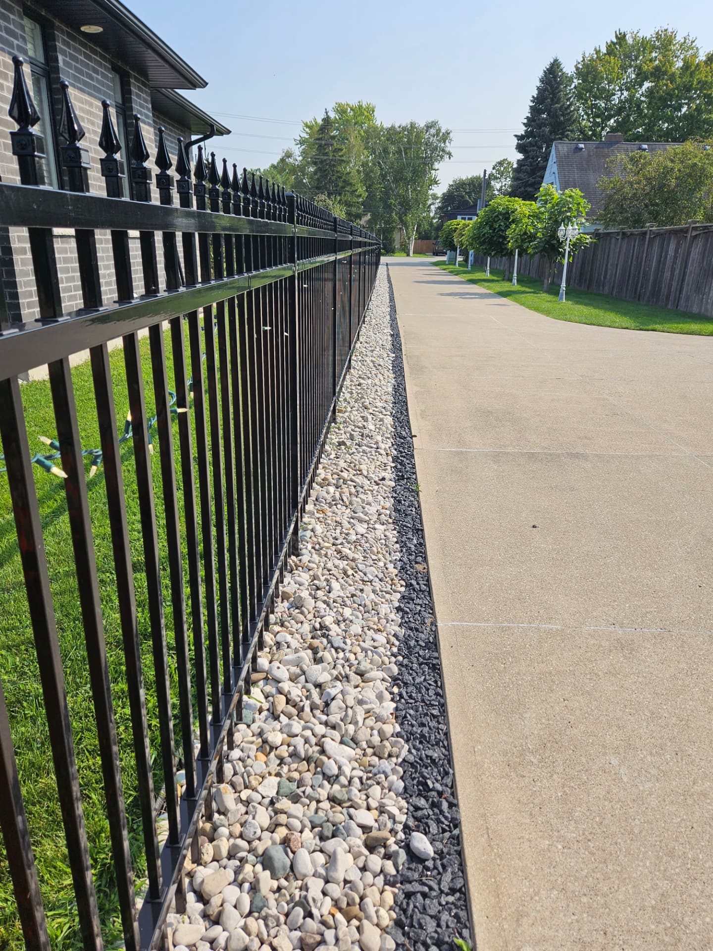 Black aluminum fence with spear-top pickets along a river-rock border beside a concrete driveway