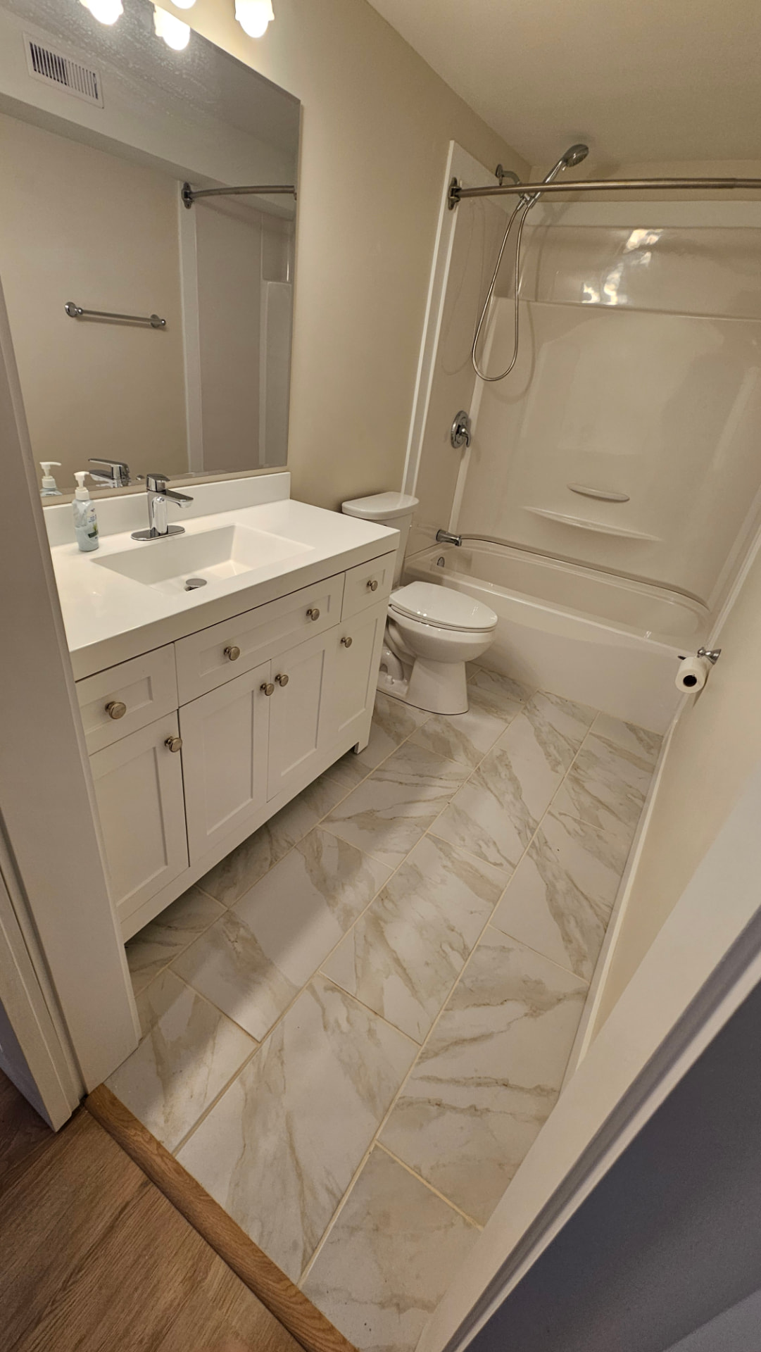 Renovated bathroom with a white vanity, marble-look tile floor and bathtub