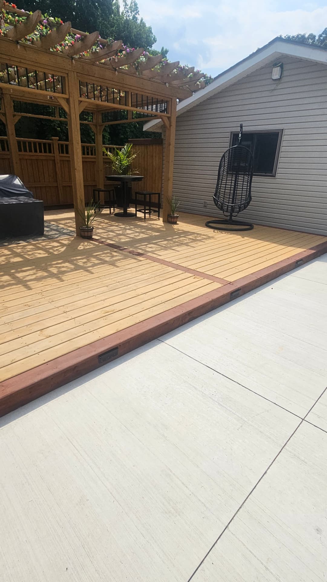Cedar deck with contrasting border boards and a hanging egg chair beside the pergola