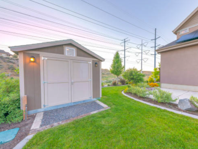 Grey garden shed with double doors, gable vent and gravel apron beside a lawn