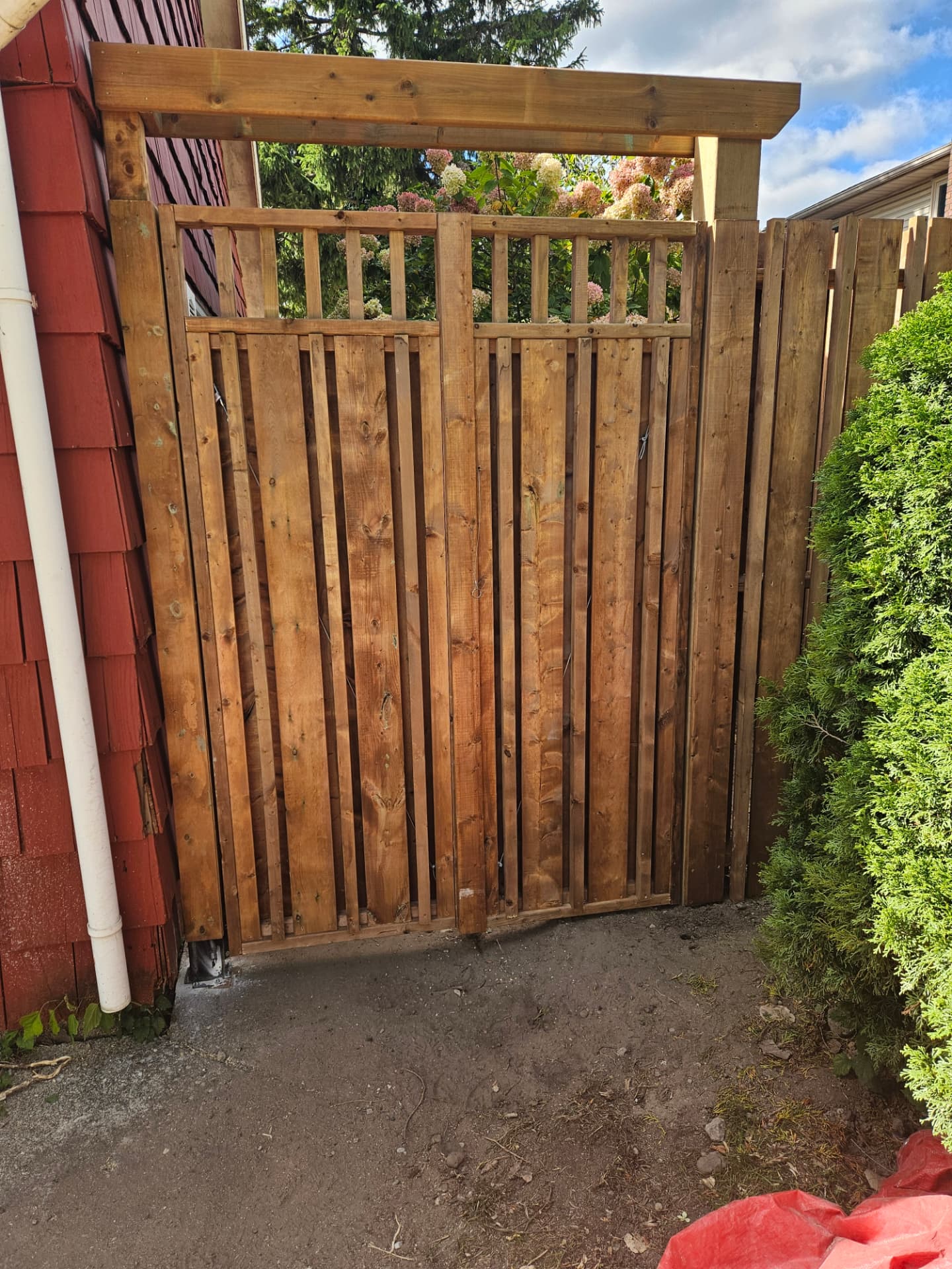 Custom cedar double gate with an open spindle top beside a home