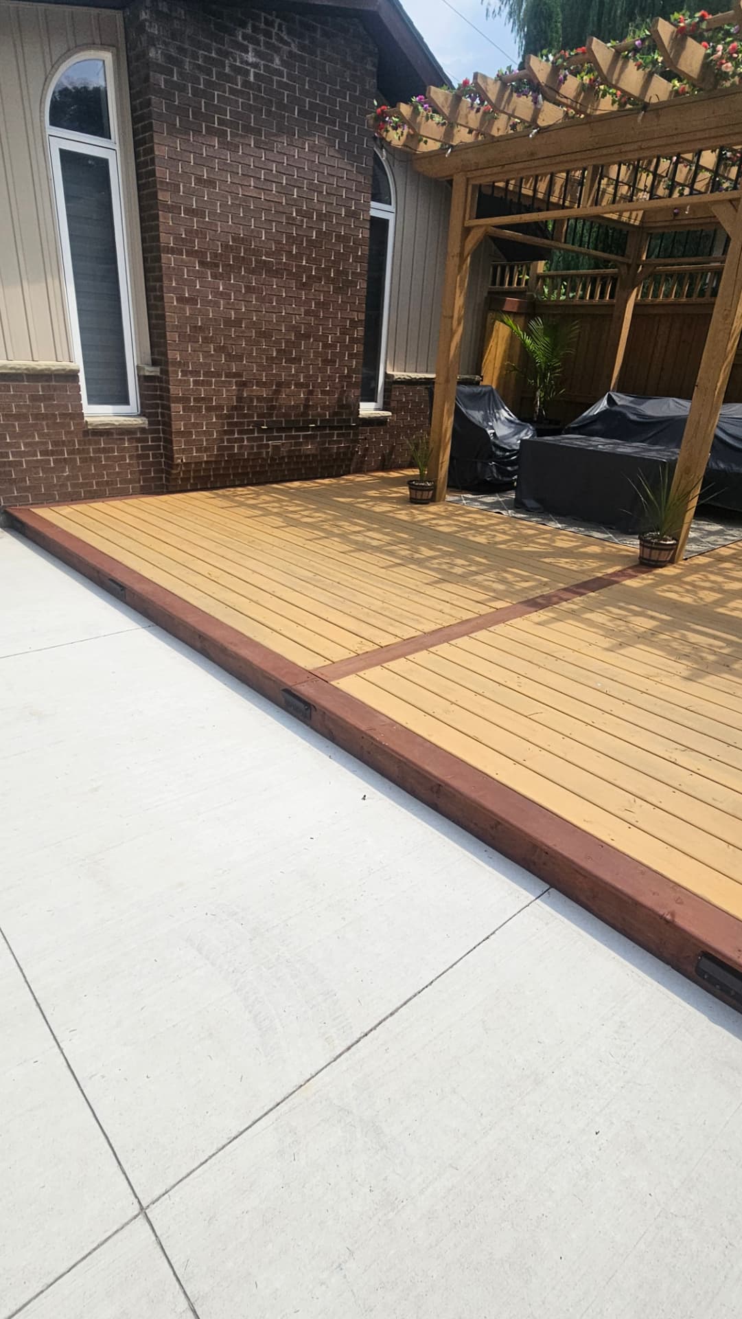 Ground-level cedar deck with a dark red border running along the brick house