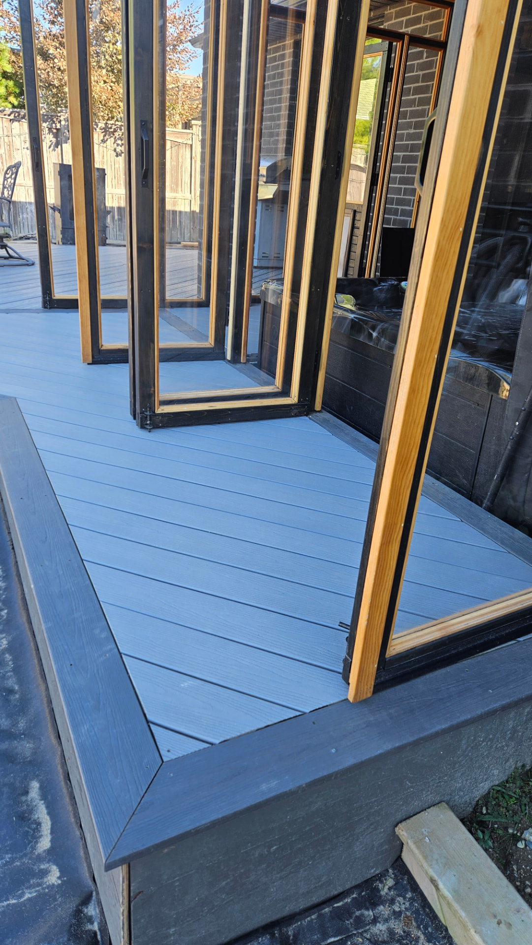 Grey composite deck with mitred dark border and folding glass doors onto a hot tub