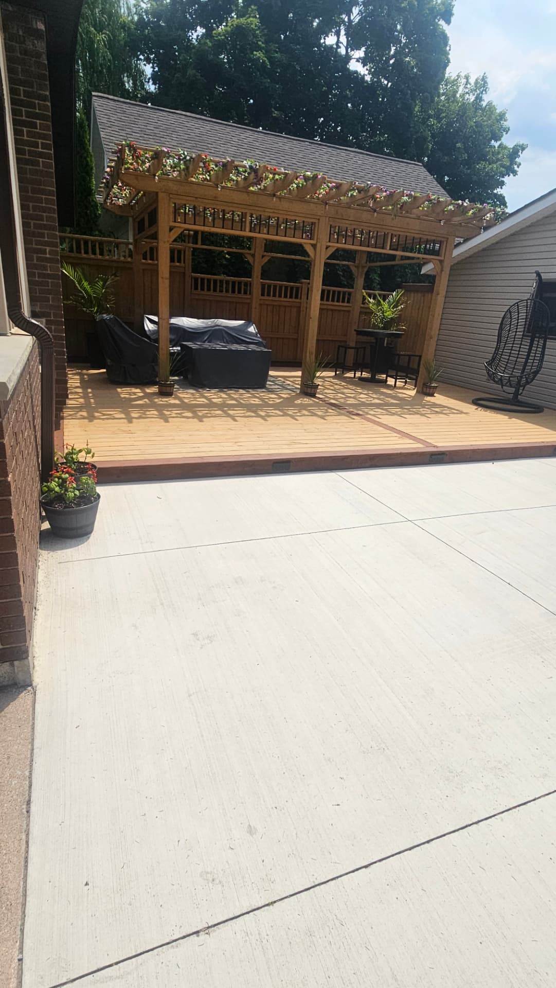 Wide view of a large cedar deck with a flower-topped pergola and hanging chair